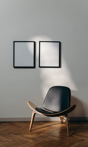 Ein Stuhl vor einer weißen Wand, an der leere Bilderrahmen hängen